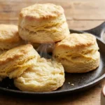 Stack of tall, flaky buttermilk biscuits in a cast-iron skillet with visible pull-apart layers and golden tops