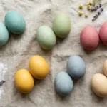 Easter eggs dyed with natural dyes and baking soda in soft teal, sage, rose, gold, and blue tones arranged on linen cloth — colors achievable only with alkaline baking soda method