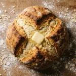Freshly baked Irish soda bread loaf on a wooden board with a deep cross score and melting butter