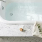 Overhead view of a white bathtub with baking soda, a linen towel, and eucalyptus on a marble surface